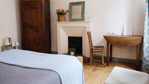 Une chambre à coucher comprenant un lit, une armoire en bois, une cheminée, une chaise, une petite table et un miroir.