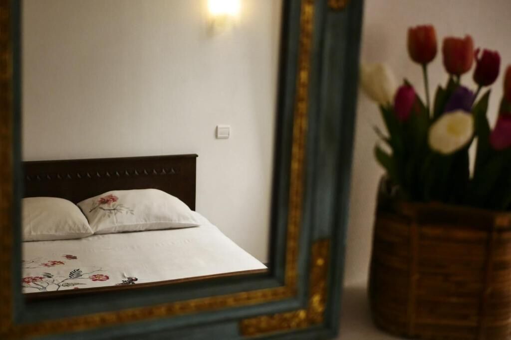 Una cama con ropa de cama floral y un espejo que refleja una pared y un jarrón de tulipanes.