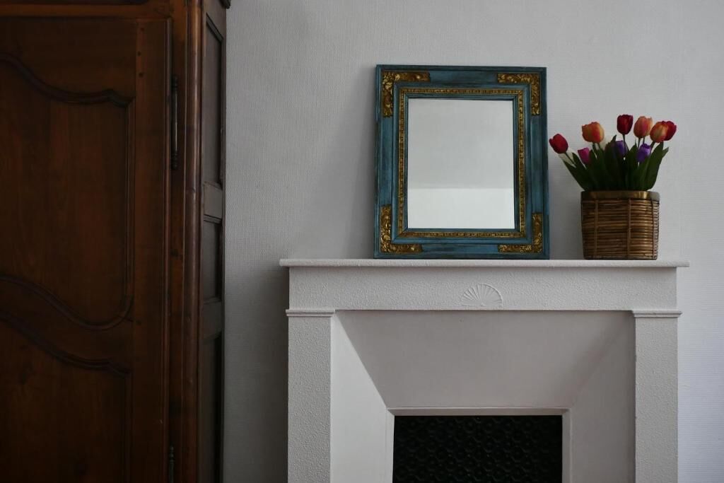 Een witte open haard met een decoratieve spiegel en een mand vol tulpen.