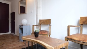 Une pièce avec une table en bois, deux chaises en bois, une petite plante en pot, une lampe et un miroir au mur.