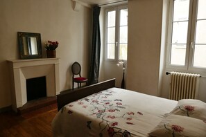 Ein Schlafzimmer mit Bett, Kamin, Sessel, Fenster und Heizkörper.