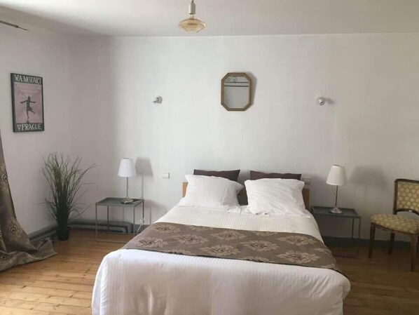 A bedroom with a large bed, two bedside tables with lamps, a chair, a mirror on the wall, and a poster on the wall.