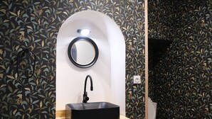 Une salle de bain avec un lavabo noir, un miroir rond et des toilettes.