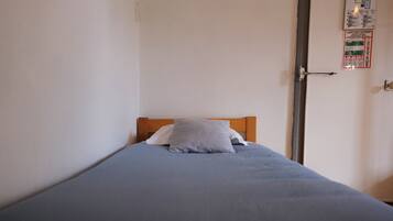 A single bed with a wooden headboard, a blue mattress, and two pillows.