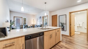 A modern kitchen with wooden cabinets, a stainless steel dishwasher, and pendant lighting. - Spacious Modern 1BR 1BA w/ AC | Downtown Redmond (Redmond)
