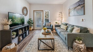 A living room with a TV, sofa, coffee table, and decorative items. - Spacious Modern 1BR 1BA w/ AC | Downtown Redmond (Redmond)