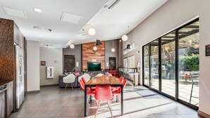 A modern dining area with a wooden table and red chairs, a grey sofa, and a large window offering a view of the outdoors. - Spacious Modern 1BR 1BA w/ AC | Downtown Redmond (Redmond)