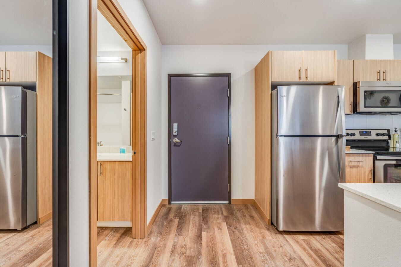 Een moderne keuken met roestvrijstalen apparatuur, houten kasten en een centrale deur.