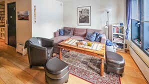 A living room with a sofa, two armchairs, a coffee table, and a rug. There is a bookshelf and a radiator.