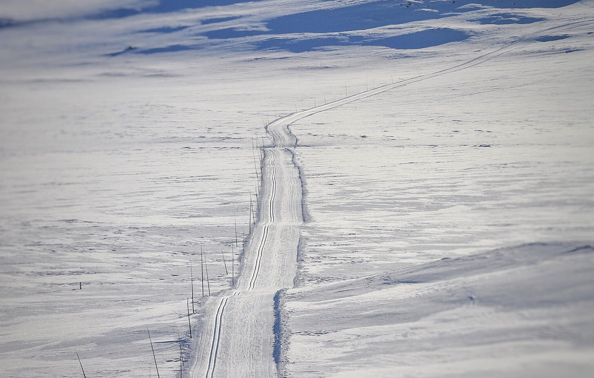 Een besneeuwde weg met een parallel daaraan lopende afrastering.