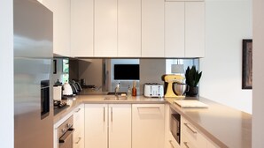 Une cuisine moderne avec des meubles blancs, un four encastré, une machine à café, un grille-pain et un mixeur jaune.