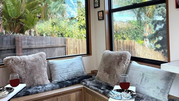 A cozy corner seating area with a view of a garden through large windows. - ArtNest: Full Kitchen & bath, Dishwasher, W/D, Firepit, Private, Parking, Safe (Escondido)