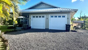 Ein zweistöckiges Haus mit Garage, umgeben von einem Schotterweg und Palmen.