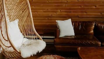 Una habitación con una silla colgante, un sofá de cuero marrón y una alfombra estampada.