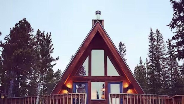 A wooden cabin with a steeply pitched roof, a wooden deck, and a ladder leading to the entrance.