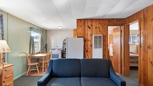 A compact living space with a sofa, wooden walls, a dining area with chairs, a table, and a kitchenette. - "B" Bear Cabin - South Fork (South Fork)