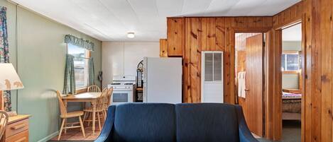A compact living space with a sofa, wooden walls, a dining area with chairs, a table, and a kitchenette.
