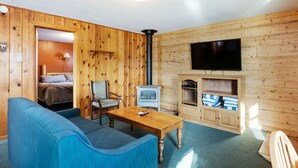 Ein gemütliches Zimmer mit Holzvertäfelung, einem blauen Sofa, einem Holztisch, einem Fernseher und einem Kamin.