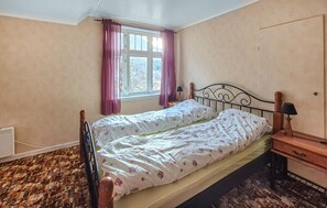 Et soveværelse med en enkelt seng, et vindue med gardiner, et natbord med lampe og en radiator.