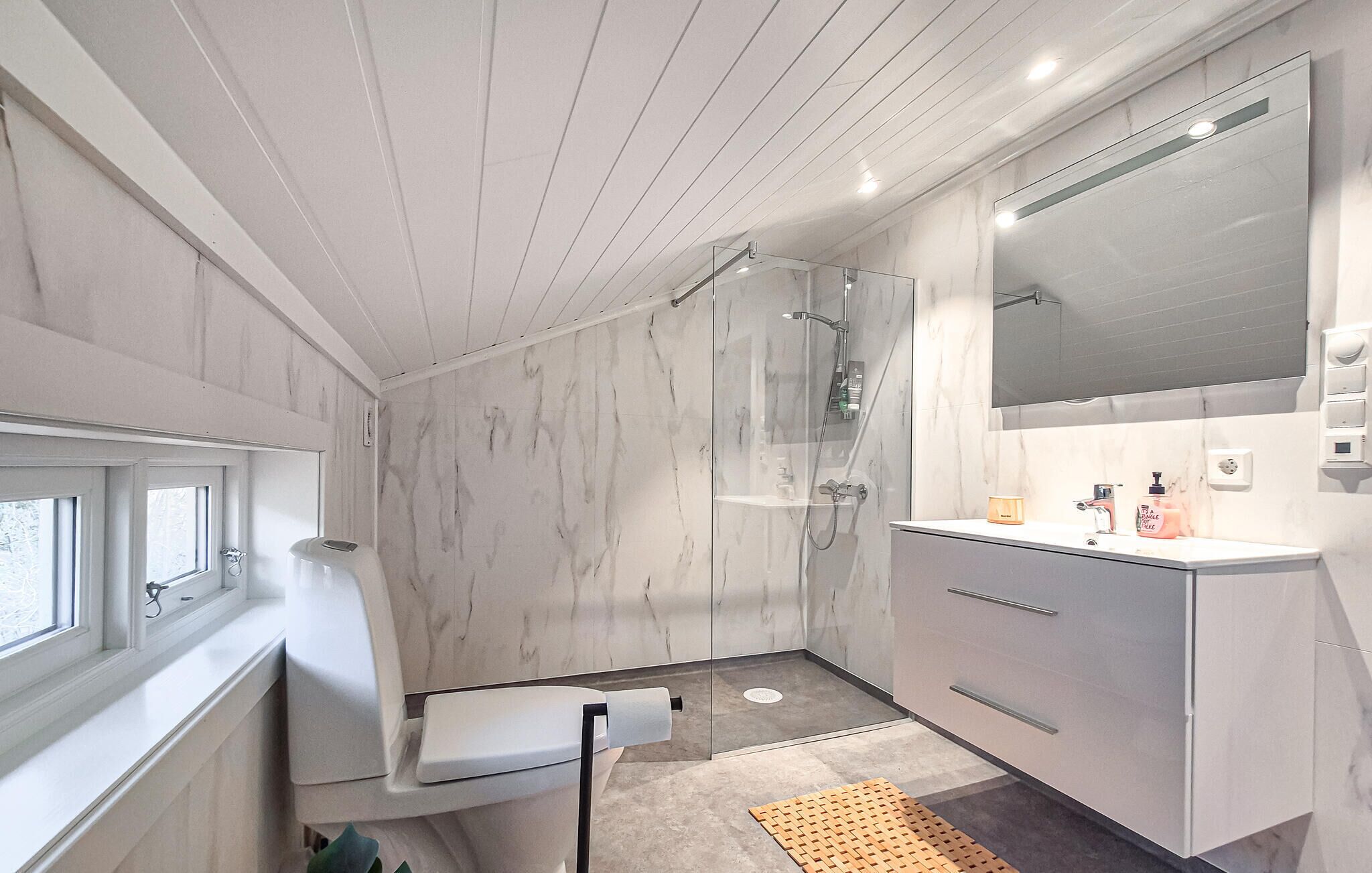 A modern bathroom with a glass shower enclosure, a large mirror, and a vanity with a sink and toiletries.