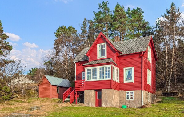 Et rødt træhus med et stejlt tag, et lille skur og en græsplæne.