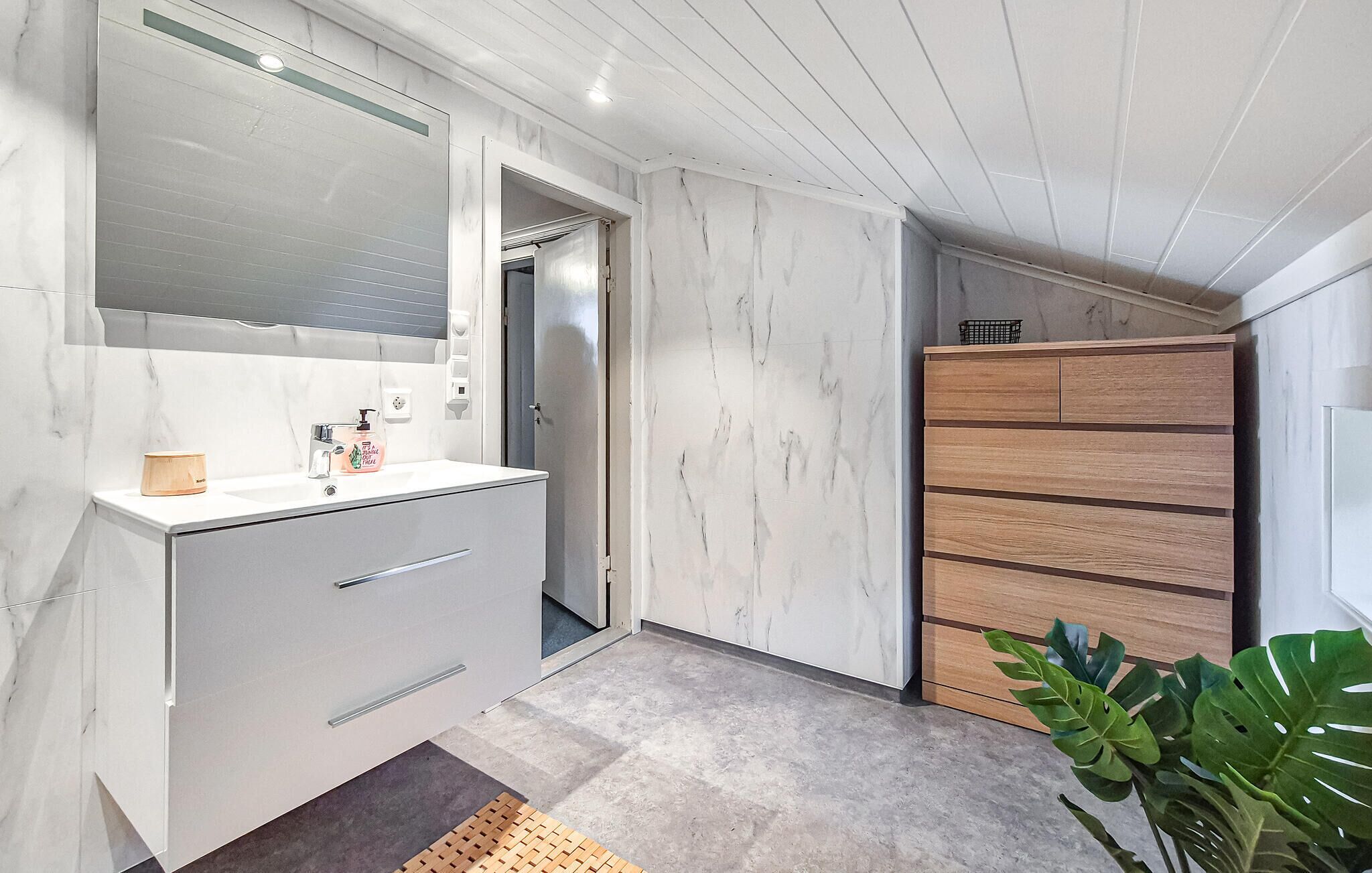 A modern bathroom with a white marble vanity, a wooden cabinet, and a large mirror.