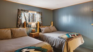 Ein Schlafzimmer mit zwei Betten, einem Fenster mit Vorhängen, einem Nachttisch mit Lampe und einer Wand mit Holz-Kopfschild.