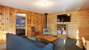 Ein gemütliches Zimmer mit Holzvertäfelung, einem an der Wand montierten Fernseher, einer Couch, einem Tisch und einem Stuhl.