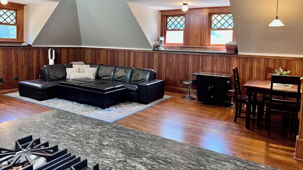 A modern living room with a sectional sofa, a dining area with a table and chairs, wooden paneling, and large windows with decorative glass panes. - Stunning Coach House in Evanston, near Lake and Northwestern University (Evanston)