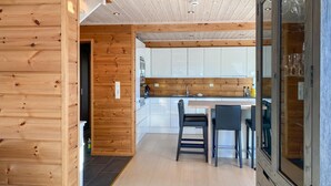 A modern kitchen with wooden paneling, a dining area with two chairs, and a glass door leading to another room. - Cozy home in Stryn with sauna (Stryn)