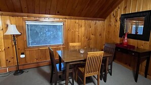 Una habitación con paneles de madera, una mesa de comedor y sillas, una lámpara, una ventana y un espejo.