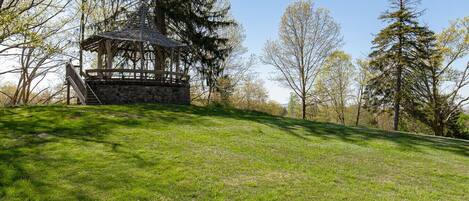 A gazebo on a grassy hill with trees in the background.