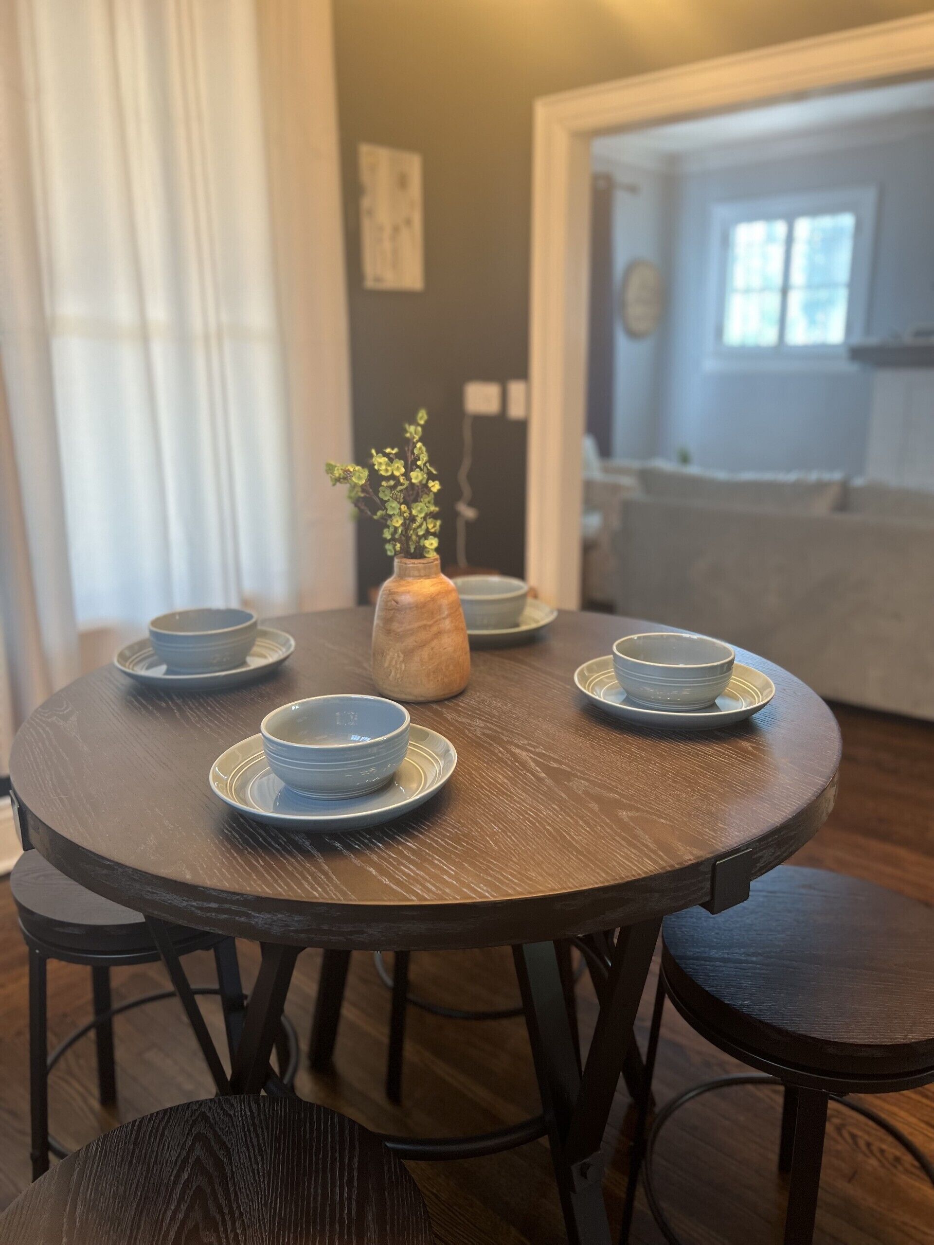 A round wooden dining table with four bowls and a vase with flowers. - Historic 3 Bedroom home, steps away from the Capitol, Clay Center and Ballpark. (Charleston)