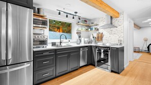 Una cocina moderna con electrodomésticos de acero inoxidable, vigas de madera y un ventanal amplio.