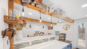 Cocina moderna con una isla grande, vigas de madera, lámparas colgantes y vistas al exterior.