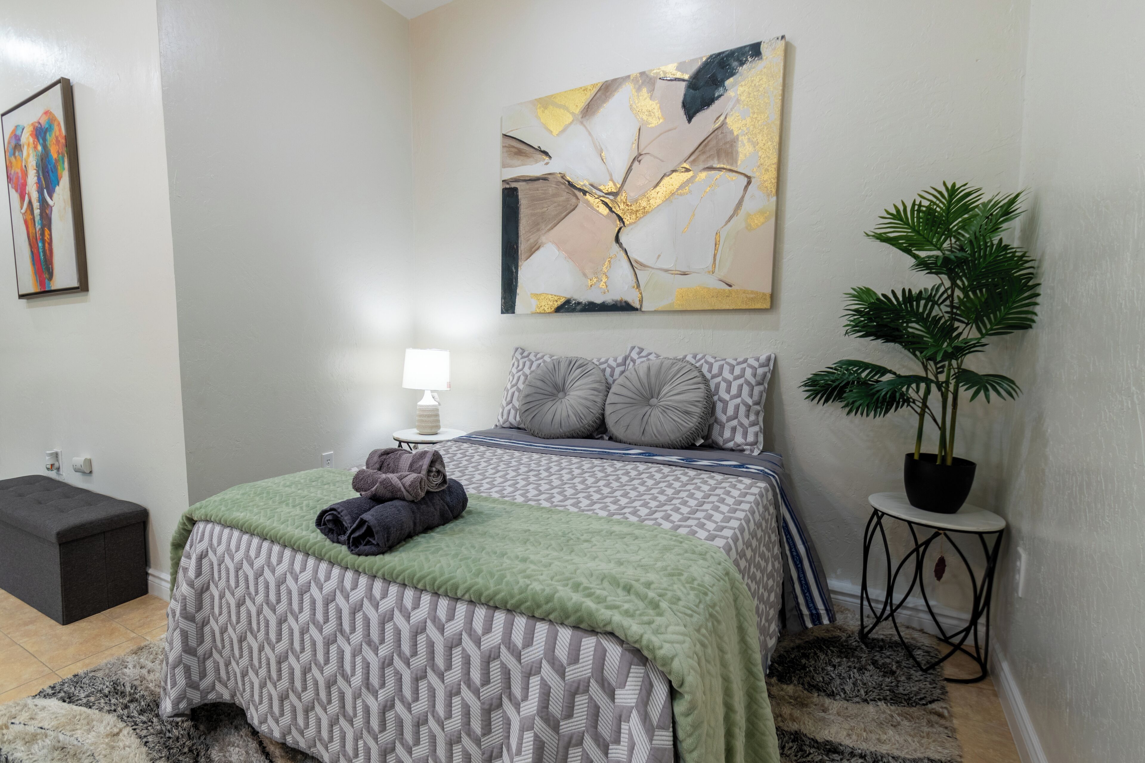 A modern bedroom with a patterned bedspread, a green throw blanket, and a potted plant.