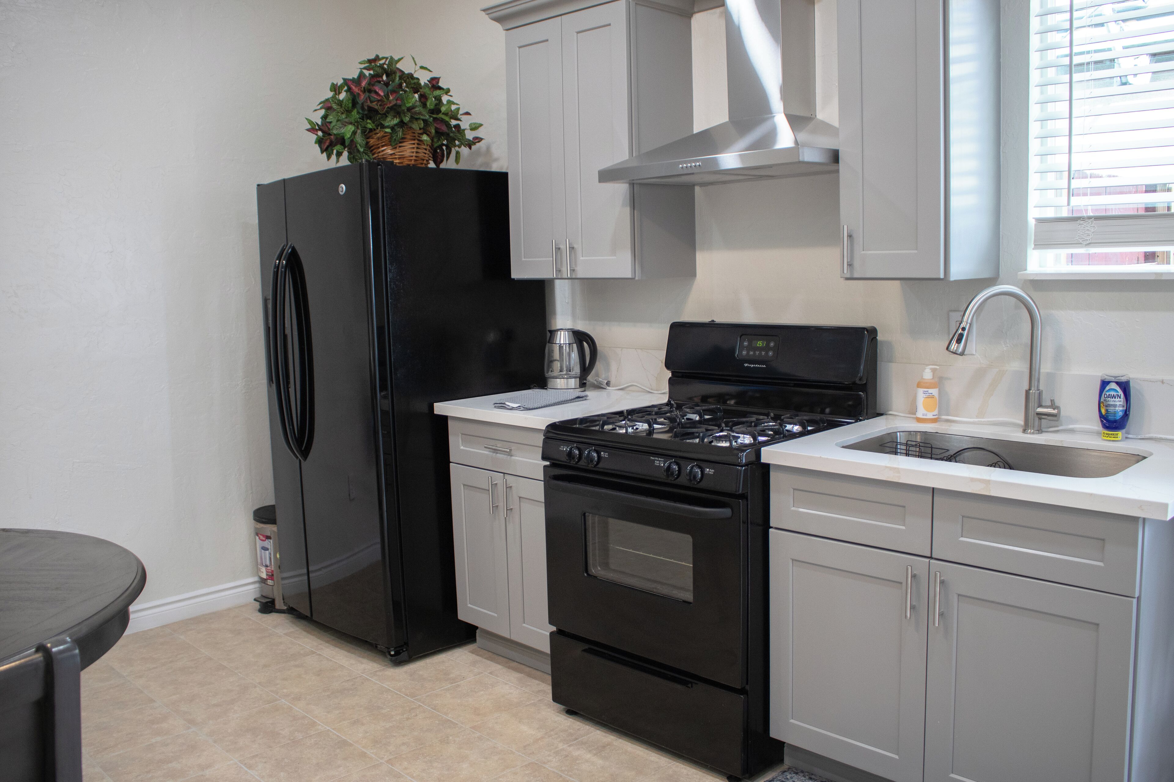 A kitchen with a black refrigerator, a stove, and a sink.