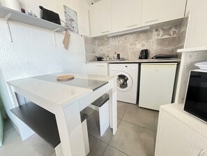 Compact kitchen with washing machine, white cabinetry, and a geometric-patterned backsplash.