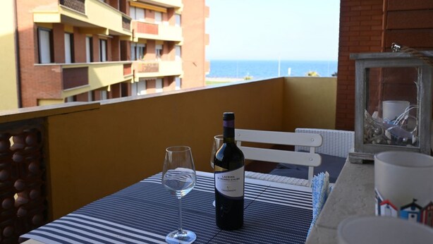 A balcony with a table, a bottle of wine, and a glass. - P051 – Porto Recanati, comfortable two-room apartment with sea view (Porto Recanati)