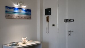 A bathroom with a white sink, a seashell, a painting of a beach, a telephone, and a door with a lock. - P051 – Porto Recanati, comfortable two-room apartment with sea view (Porto Recanati)