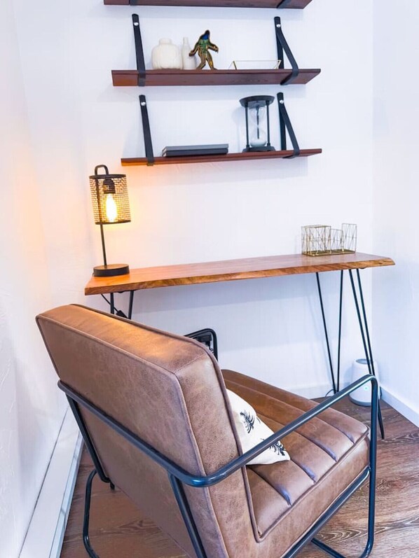 Una habitación moderna con una butaca de cuero marrón, un escritorio de madera y dos estanterías con objetos decorativos.