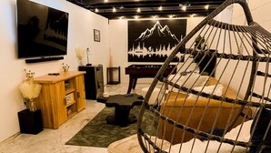 A cozy room with a hanging chair, a pool table, a flat-screen TV, and a mountain mural on the wall.