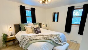 A bedroom with a bed, bedside tables, a nightstand, a window with curtains, a ceiling light, and a patterned rug.