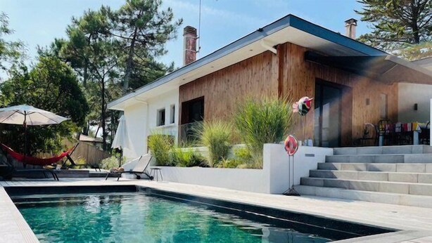 Una casa moderna con piscina, terraza de madera y zona de estar exterior.