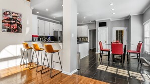 A modern kitchen with white cabinets, a central island, and a dining area with red chairs. - New! Lux Mansion, 5 BR 4 BA, Heated Pool, Sleeps 12+ (Fayetteville)