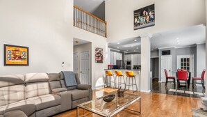 A spacious living room with a grey sectional sofa, a glass coffee table, and a dining area with a red table and yellow chairs. - New! Lux Mansion, 5 BR 4 BA, Heated Pool, Sleeps 12+ (Fayetteville)