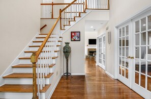 Un escalier avec des marches en bois et une rampe blanche, menant à une pièce dotée d’une cheminée et d’un lit.