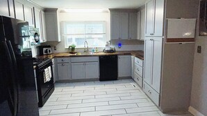 A kitchen with white cabinets, a black refrigerator, and a tiled floor. - The Beauty Lounge Guest House (Manchester)