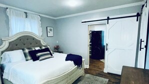 A bedroom with a bed, a nightstand, a dresser, and a door leading to another room. - The Beauty Lounge Guest House (Manchester)