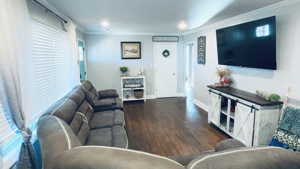A living room with a sectional sofa, a flat-screen TV, and a small cabinet. - The Beauty Lounge Guest House (Manchester)